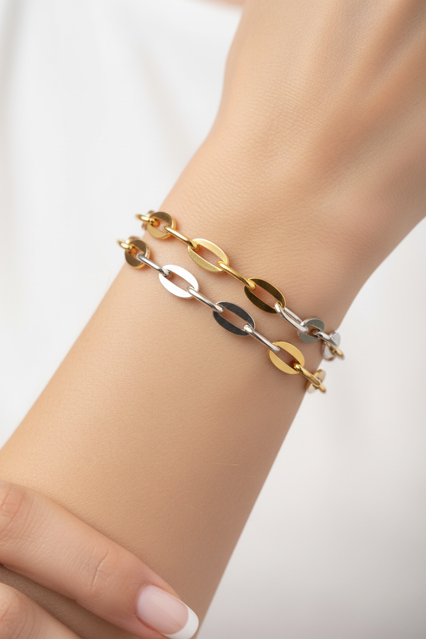 Multiple gold and silver chain bracelet styles stacked on wrist in sunlight